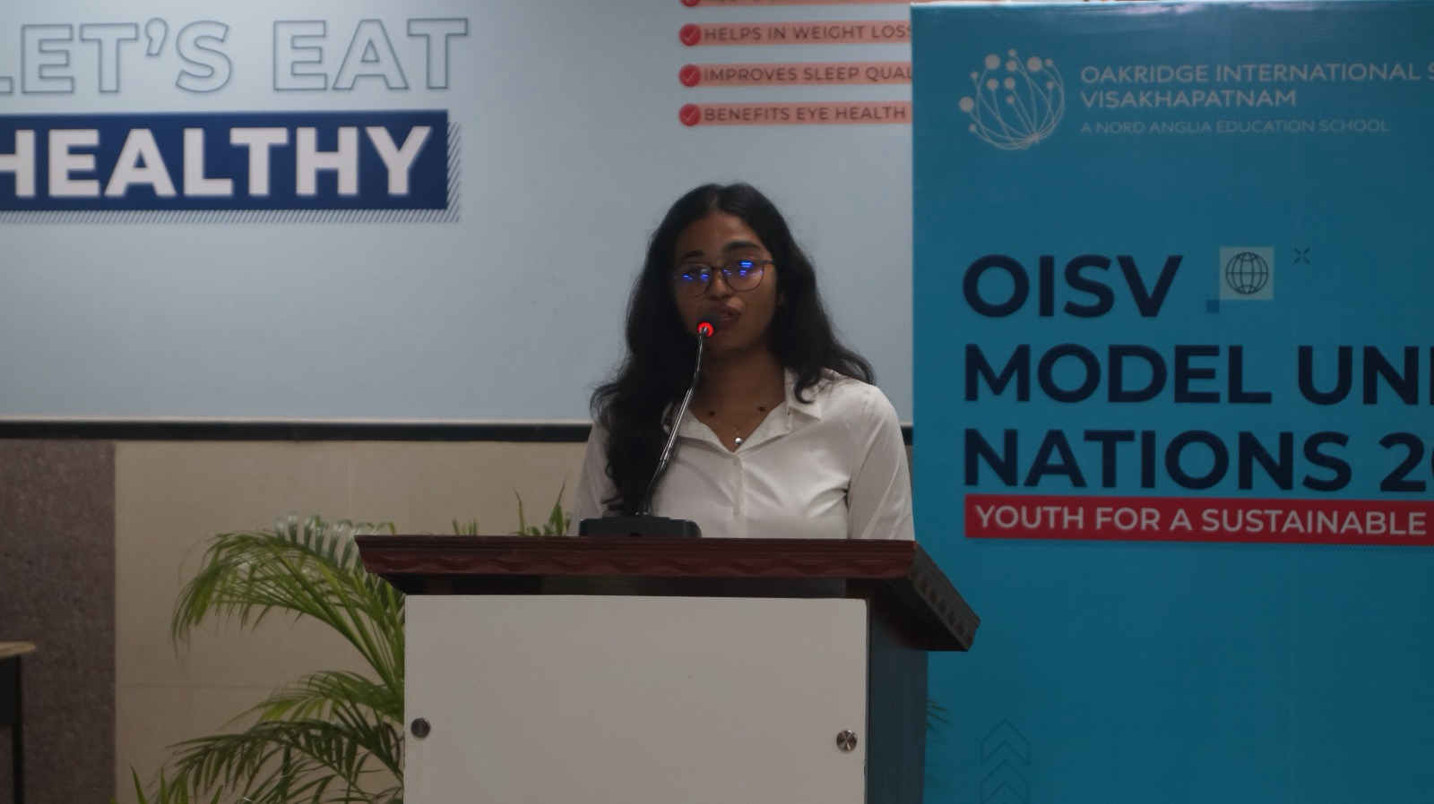 Speaker at the podium beside OISV MUN event signage